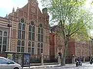 Colour photograph of the Grade II listed school building at Cheltenham Road, Montpelier, Bristol. The building is constructed from red bricks, with yellow brick and terracotta dressings, and a slate roof. The building is shown with three storeys and fourteen windows, facing a road with trees obscuring the view in the foreground.