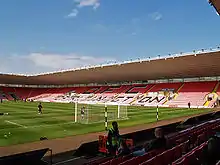 Inside an almost-empty modern stadium whose coloured seats spell out the initials D F C and the word Darlington. Players appear to be warming up on the pitch.