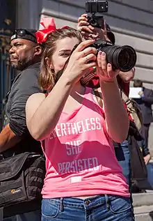 Woman wearing a pink T-shirt with Nevertheless, She Persisted printed in white