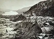 Lake beside snowy mountains with railroad construction sheds in foreground