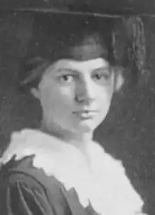 A young white woman wearing an academic mortar-board cap and a white lace-trimmed collar over an academic gown