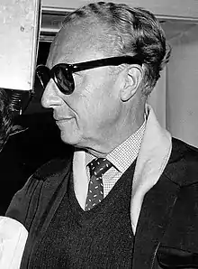 A black-and-white picture of a man wearing dark glasses and a spotted tie. His head is facing toward the left.