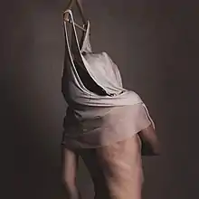 The upper half of a person whose head is covered by a piece of clothing hanging on a hanger