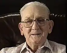 Colour photo of Ross, a white man in his 90s with white hair. He is wearing glasses and a collared shirt.