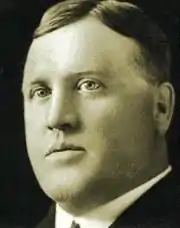 Black and white photo of a man aged 27, clean-shaven, wearing a white dress shirt and a dark suitcoat