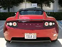 Photograph of a parking space with the words "SpaceX" and "reserved". The parking space contains a red convertible sports car with Californian license plate TSLA 10. On the rear of the vehicle are written the words "Tesla Roadster Sport".