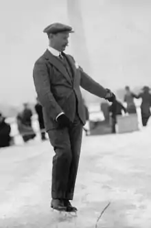 Photo of a man wearing a suit, gloves and ice skates on ice in front of an obelisk