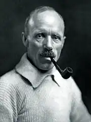 Head and upper body of a man, balding, smoking a pipe. He is wearing a heavy jersey.