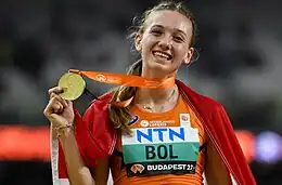 Photo of Femke Bol with a flag draped over her shoulders and holding a gold medal