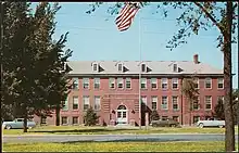 A three-story red brick building from the early 20th century, as seen on a 1950s postcard