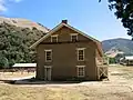 East end of the restored barracks building.  The unreconstructed kitchen/mess hall is outlined by split rail fence to the left.