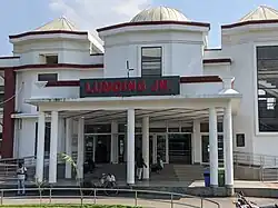 White train station building with wide steps leading up to the entrance and a sign reading "Lumding Jn." in large, red letters.