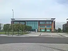 A wide orange rectangular building with turquoise windows, partly obscured on the left by rows of trees and a road light