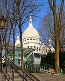 A photograph of the upper station of the funicular from below, with the Basilique du Sacré-Cœur prominently behind it.