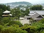 Trees and a raked sand garden next to traditional Japanese buildings.