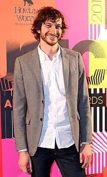 A man wearing a grey suit smiling for cameras.