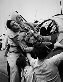 Crewmen aboard USS Saratoga lift a wounded aviator out of a Grumman TBF Avenger's rear turret.  Photo by Lt Wayne Miller.