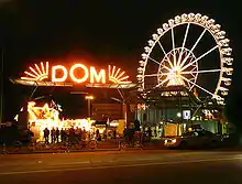 A red lighted sign with the word Dom and a lighted Ferris wheel in the background.