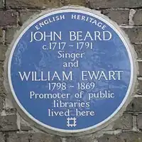 A Blue plaque on a brick wall with the words "John Beard C1717 – 1791 Singer and William Ewart 1798 – 1861 Promoter of Public Libraries