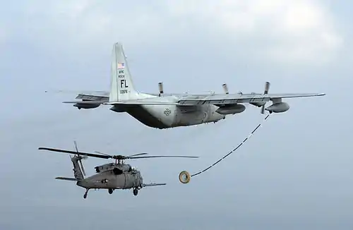 Helicopter with refuelling probe approaching the drogue trailed by a tanker.