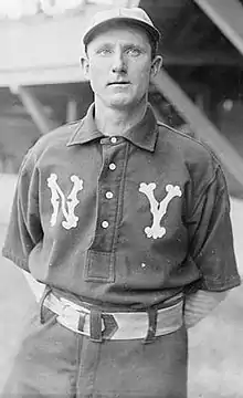 A man wearing a gray baseball uniform with white "NY" on opposite sides of the chest and white baseball cap