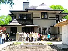 A recent straight on shot of the west elevation taken from the far end of the backyard. The new garage is visible at right. A large group of people in the backyard are taking part in the Wright Plus 2009 Home tour.