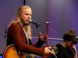 Two members of the band seen sitting onstage, playing their respective instruments