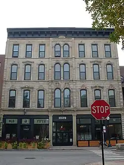 An off-white stone building with a black cornice, in head-on view