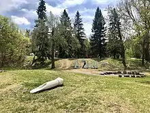 Indigenous Art Park, ᐄᓃᐤ (ÎNÎW) River Lot 11 on a spring day with mikikwan by Duane Linklater in the foreground - a large concrete sculpture of a buffalo bone hide scraper