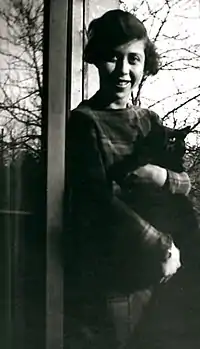 Black and white photo of a smiling young woman with a mass of dark hair and a large black cat in her arms.