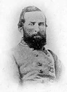 Black and white grainy photo shows a dark bearded man wearing a gray military uniform.