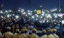 Students use their mobile phone flashlights to illuminate their protest after street lights are turned off by power company TNEB.