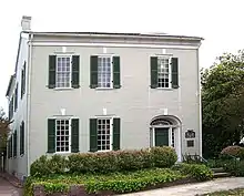 A two-story brick building with large windows and shrubbery in front of it