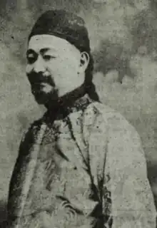 A Chinese man with a goatee, wearing a brimless cap and a traditional quilted jacket