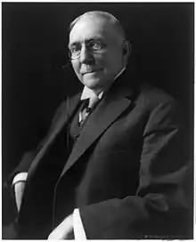 Man wearing large round glasses sits back in a chair