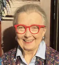 A smiling older white woman with red glasses