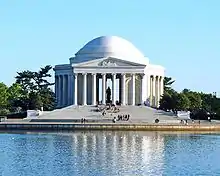 Round white memorial with columns and dome in front of the water