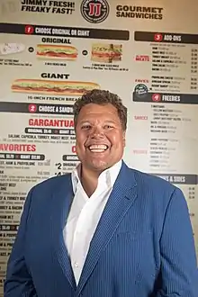 Headshot of Jimmy John Liautaud in 2018 in front of a Jimmy John's menu