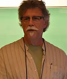 This image is of John Barber, speaking in front of a green backdrop.