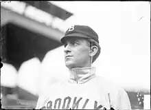 A man wearing a baseball cap and jersey with "Brooklyn" written across the chest looks to the the left.