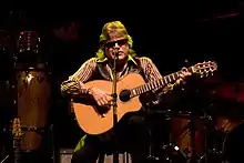 A man is sitting on a stool playing a guitar.