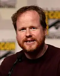 A man with brown hair in a dark red shirt talking into a microphone.