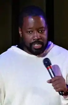 A man wearing a white/grey shirt is talking into a microphone.