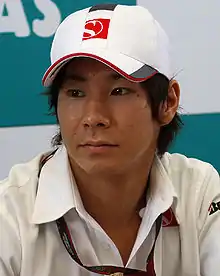 A portrait of a man in his mid-20s wearing a white T-shirt and baseball cap with the logo of the Sauber Formula One team looking to the right of the camera.