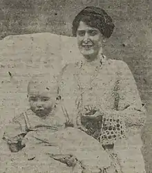 Black and white portrait of a dark haired women wearing a white dress holding a baby boy