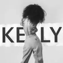 An image of an African-American woman. She is topless and hugging herself while turned away from the camera. The word "Kelly" is placed behind the woman.