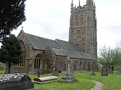 Gray stone building with ornate square tower and slate roof. In the foreground are gravestones