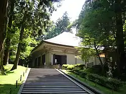 A building with pyramid shaped roof at the end of a flight of stairs.