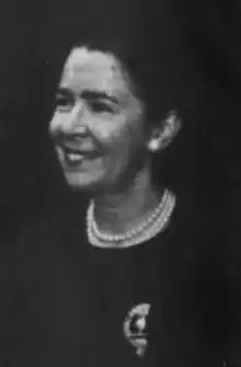 A smiling white woman with dark hair, wearing pearls