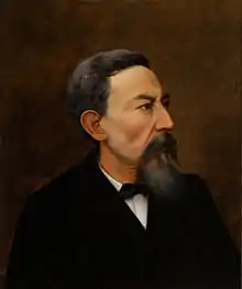 Color portrait of a bearded man wearing a black suit, facing right.